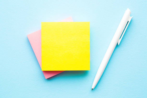 Bright yellow and pink sticky notes and white pen on light pastel blue table. Empty place for message, quote, sayings or other text for positive mood.