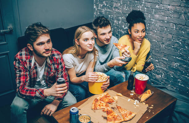 istock Excited young people are sitting together on a couch, eating popcorn and watching different movies. They are concentrated only on that. 1147486131