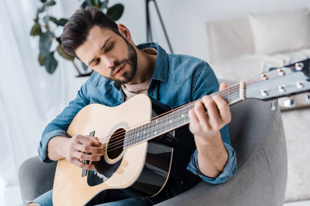 istock handsome bearded man playing acoustic guitar at home 1147492483