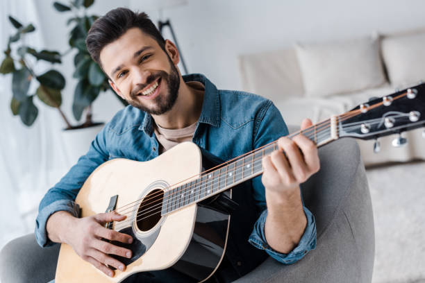 istock cheerful bearded man playing acoustic guitar at home 1147492490