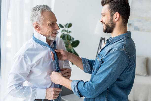 istock cheerful handsome son helping elegant retired father tying blue tie at home 1147492584