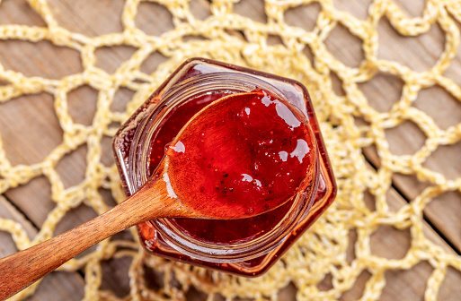 Close-up wooden spoon full of homemade strawberry jam on yellow knitted napkin on wooden table. Natural homemade dainty.
