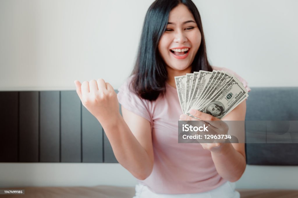 Close-Up Portrait of Attractive Woman Holding Money Cash From Savings With Happy Expression on Her Bedroom. Business Financial and Savings Concept Close-Up Portrait of Attractive Woman Holding Money Cash From Savings With Happy Expression on Her Bedroom. Business Financial and Savings Concept. Currency Stock Photo