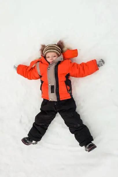 Happy little boy child laying on snow and making snow-angel