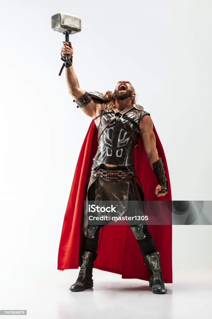 Man in cosplaying Thor isolated on white studio background Long hair and muscular male model in leather viking's costume with the big hammer cosplaying Thor isolated on white studio background. Full-lenght portrait. Fantasy warrior, antique battle concept. Hammer Stock Photo