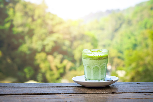 Green tea or Matcha latte in a glass on the wooden table on nature landscape background