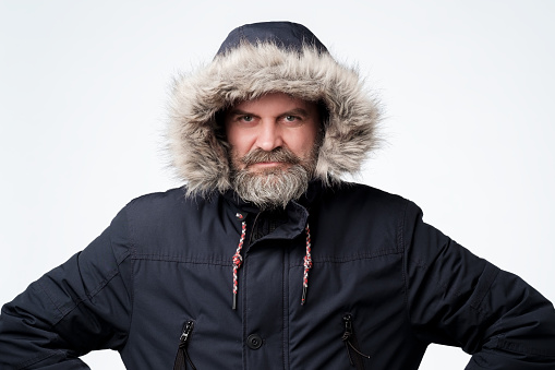 Mature caucasian man with beard in winter jacket with hood. Prepared for weather changes.