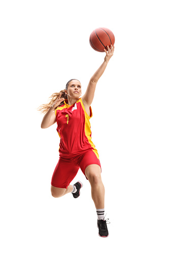 Full length portrait of a female basketball player jumping with a ball isolated on white background