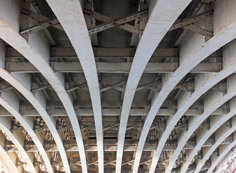 perspective view of curved arch shaped steel girders under an old road bridge with rivets and struts painted grey