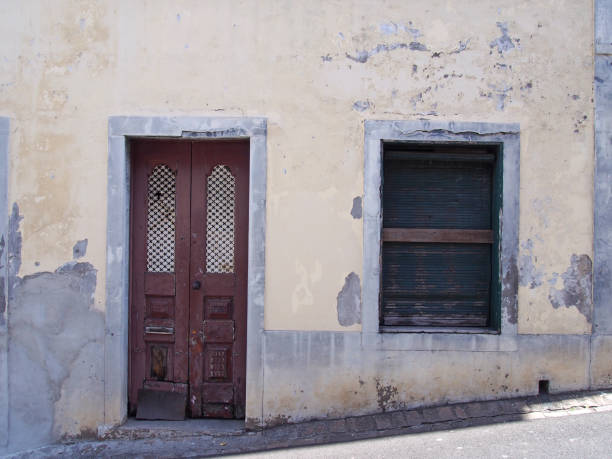 istock a run down empty abandoned house with crumbling yellow painted walls barred closed shutters and a broken wooden door on a sloping street in funchal portugal 1147516827