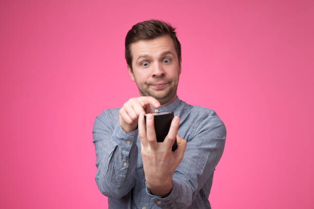 istock young man standing, using smartphone and watching video with amazed face. 1147517783