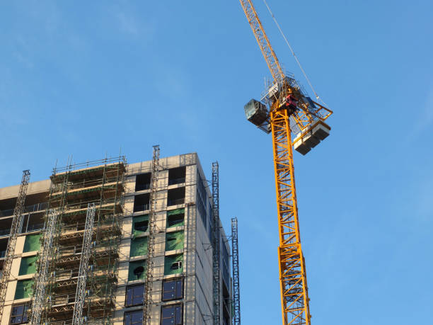 istock large modern building under construction covered in scaffolding with a tower crane against a bright blue sky 1147517944
