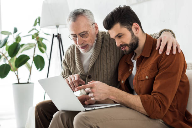 istock handsome bearded man pointing with finger at laptop while sitting with senior father 1147518407
