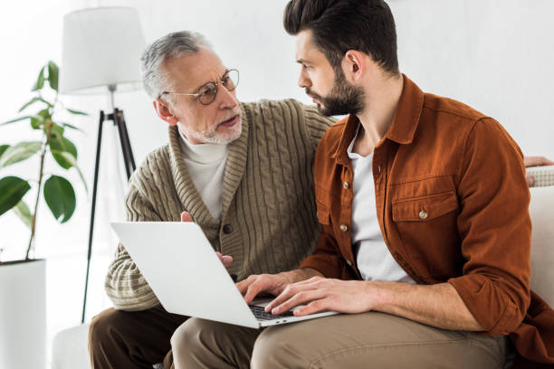 istock senior father looking at bearded son sitting with laptop 1147518415
