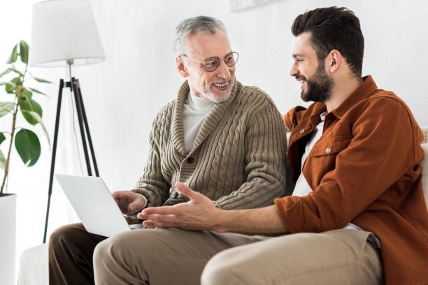 istock happy bearded man gesturing while sitting with senior father and looking at laptop 1147518416