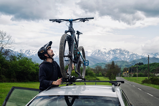 Young Man attaching bike to a roof carrier, mountains in background.