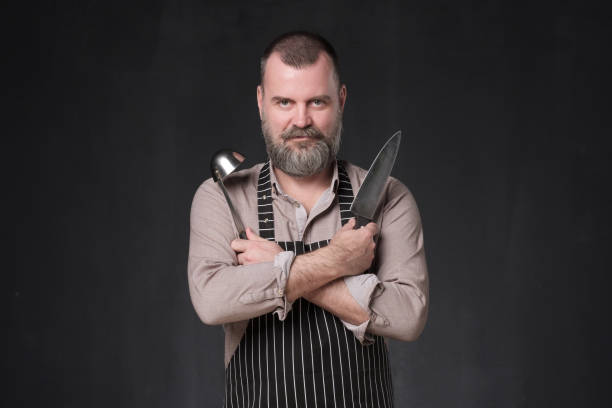 istock Mature european chef with beard holding a ladle standing on black studio wall. 1147519981