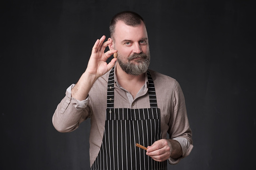 Mature man in apron showing cinnamon spices. Giving advice how to cook. Studio shot