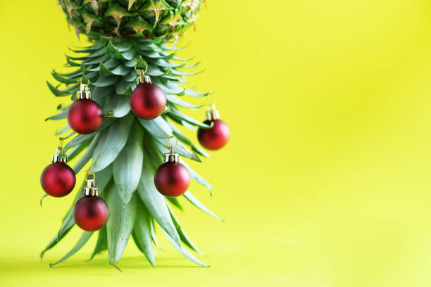 istock Creative Christmas tree made of pineapple and red bauble on yellow background, copy space. Greeting card, decoration for new year party. Holiday concept. 1147521027