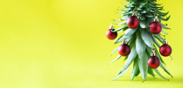 istock Creative Christmas tree made of pineapple and red bauble on yellow background, copy space. Greeting card, decoration for new year party. Holiday concept. Banner 1147521030