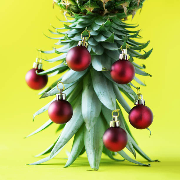 istock Creative Christmas tree made of pineapple and red bauble on yellow background, copy space. Greeting card, decoration for new year party. Holiday concept. Square crop 1147521040