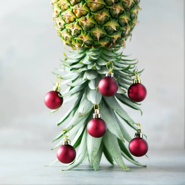 istock Creative Christmas tree made of pineapple and red bauble on grey concrete background, copy space. Greeting card, decoration for new year party. Holiday concept. Square crop 1147521083