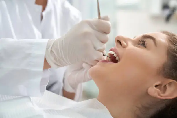 Closeup of woman lying on dental chair with open mouth and dentist in white protective gloves examining teeth. Female patient treating and caring about teeth. Concept stomatology and health.