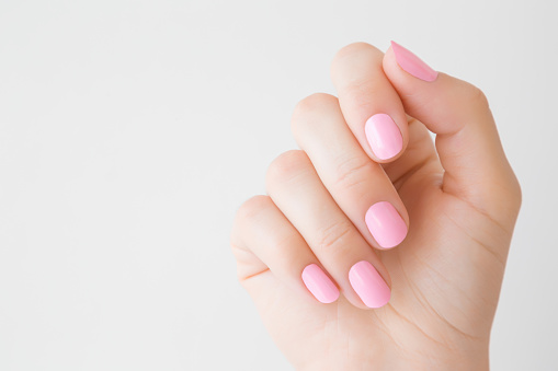 Beautiful groomed woman's hand with pink nails on light gray background. Manicure, pedicure beauty salon concept. Empty place for text or logo. Closeup.