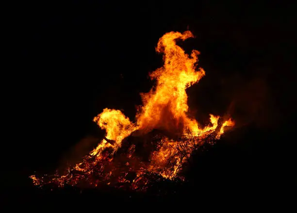 Photo of Large bonfire, burning and glowing with soft flames, sparkles flying agains the dark sky. Glowing wood silhouettes. Walpurgis night, traditional witch burning and spring welcoming ritual. 30 April.