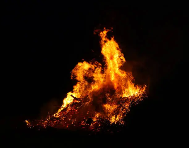Photo of Large bonfire, burning and glowing with soft flames, sparkles flying agains the dark sky. Glowing wood silhouettes. Walpurgis night, traditional witch burning and spring welcoming ritual. 30 April.