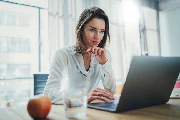 Confident businesswoman working on laptop at her workplace at modern office.Blurred background. Confident businesswoman working on laptop at her workplace at modern office.Blurred background office laptop stock pictures, royalty-free photos & images