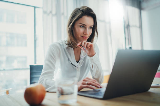 pewna siebie bizneswoman pracująca na laptopie w swoim miejscu pracy w nowoczesnym biurze. rozmyte tło. - stock market analyzing computer finance zdjęcia i obrazy z banku zdjęć