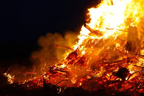 Photo of Large bonfire, burning and glowing with soft flames, sparkles flying agains the dark sky. Glowing wood silhouettes. Walpurgis night, traditional witch burning and spring welcoming ritual. 30 April.