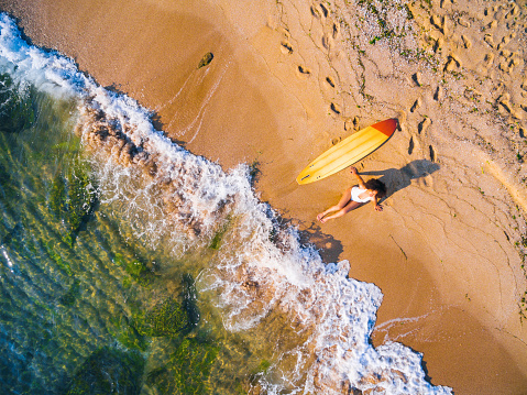 Aerial view of a surfer girl resting on a beach.