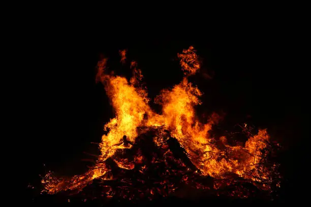 Photo of Large bonfire, burning and glowing with soft flames, sparkles flying agains the dark sky. Glowing wood silhouettes. Walpurgis night, traditional witch burning and spring welcoming ritual. 30 April.