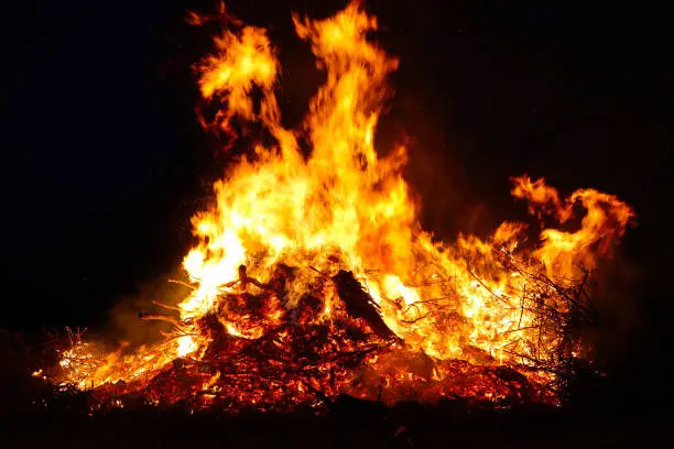 Photo of Large bonfire, burning and glowing with soft flames, sparkles flying agains the dark sky. Glowing wood silhouettes. Walpurgis night, traditional witch burning and spring welcoming ritual. 30 April.