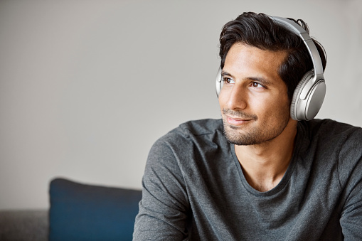 Thoughtful entrepreneur wearing headphones looking away. Male executive is listening music in creative workplace. He is sitting on sofa.