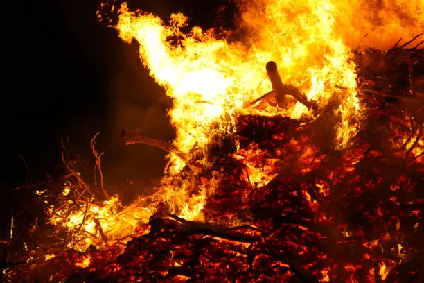 Photo of Large bonfire, burning and glowing with soft flames, sparkles flying agains the dark sky. Glowing wood silhouettes. Walpurgis night, traditional witch burning and spring welcoming ritual. 30 April.