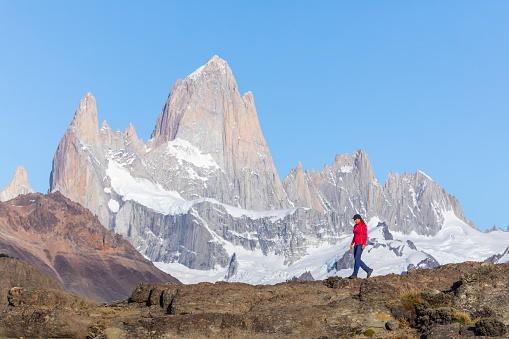 A woman is standing  on a clifftop above El Chalten looking over to Mount Fitz Roy in Los Glaciares National park