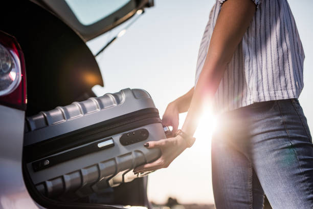 Unrecognizable woman packing her suitcase into the car trunk.