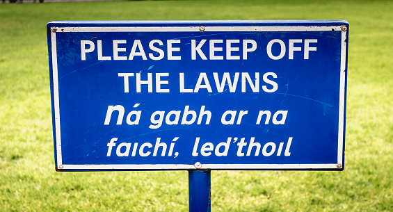 blue sign Please Keep off the Laws in English and Irish on a lawn