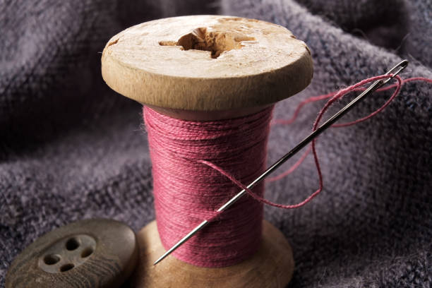 istock Sewing needle and cotton thread on wooden spool macro view. 1147541636