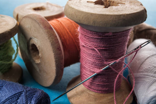 istock Sewing needle and cotton thread on wooden spool macro view. 1147541685