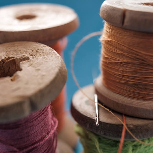 istock Sewing needle and cotton thread on wooden spool macro view. 1147541743