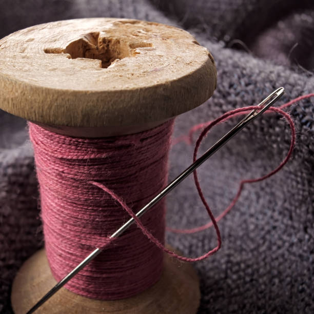 istock Sewing needle and cotton thread on wooden spool macro view. 1147541759