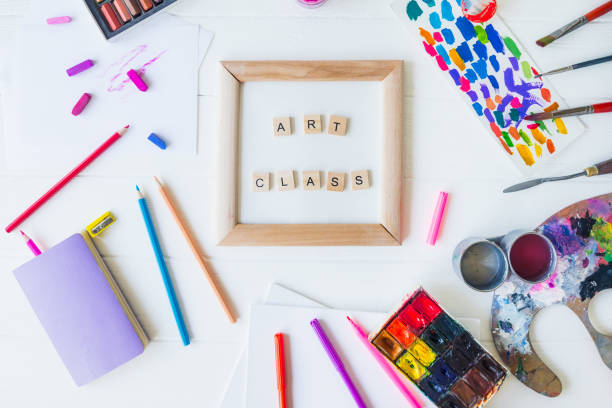 istock Top view creative art class concept. Canvas in frame with lettering inside and many colorful paintiing materials on the white wooden background. Drawing lesson for children and adults. Flat lay 1147542282