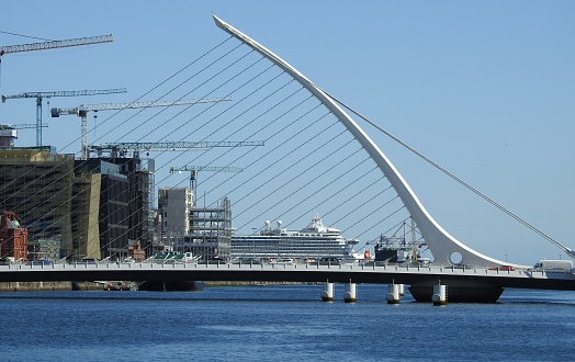 4th May 2019, Dublin, Ireland.  Cable-stayed Samuel Beckett Bridge in Dublin's Docklands, crossing over the River Liffey. A cruise ship can be seen in  the background as well as 5 construction cranes.