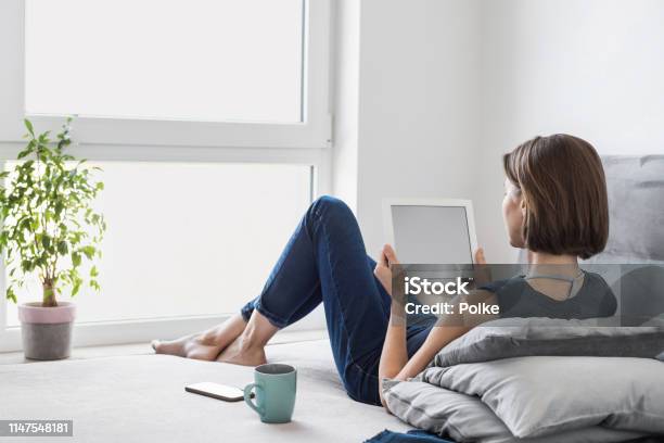 Young Woman Using Digital Tablet At Home Stock Photo - Download Image Now - Digital Tablet, Reading, Sofa