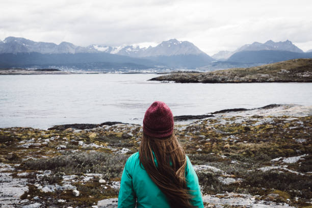 Woman exploring the Beagle Channel in Ushuaia Woman in hat and green jacket staying on the small island looking at the ocean and mountains at the end of the world, Tierra Del Fuego region, Argentina tierra del fuego national territory stock pictures, royalty-free photos & images