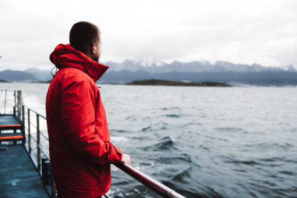 Man exploring the Beagle Channel in Ushuaia by cruise ship Man in red jacket enjoying a view of mountains, Pacific Ocean and small islands from the ship, sailing at the end of the world, Argentina beagle channel stock pictures, royalty-free photos & images